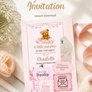 May include: A rectangular baby shower invitation card in shades of pink and gold. The design features a teddy bear with a pink bow, pumpkins, baby clothes, and blocks. Text includes A little pumpkin IS ON THE WAY!, Charlotte, October 3rd, 2026 at 4PM, 123 Peters Ln Springfield OR, 97477, Registry, and RSVP.