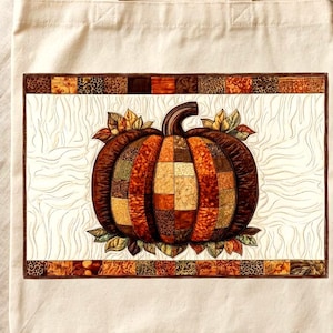 Puede incluir: Un bolso de tela color crema con un gráfico rectangular central de una calabaza. La calabaza está construida con un mosaico de patrones de tela en tonos marrón, naranja y amarillo, rodeada de hojas estilizadas y un borde de cuadrados pequeños.