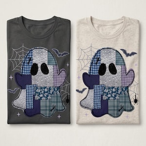 Puede incluir: Dos camisetas, una gris oscuro y otra beige jaspeado claro, cada una con un gráfico central de un fantasma hecho de parches de tela con patrones azules y morados, rodeado de telarañas, murciélagos y una pequeña araña estampados.