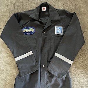 Può includere: Tuta da lavoro nera con rifiniture riflettenti sulle maniche. La tuta ha due toppe, una che dice "Material Services" e un'altra che dice "Continental".