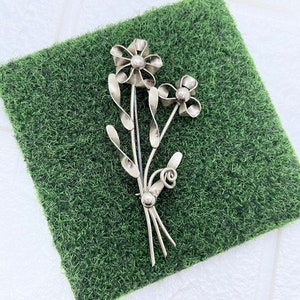 May include: A silver brooch in the shape of a bouquet of flowers. The flowers are stylised and have a simple, elegant design.