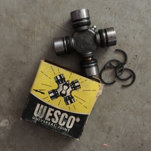 May include: A metallic universal joint with the text "USA" stamped on it, alongside a yellow and black box labelled "WESCO UNIVERSAL JOINT". Three retaining rings are also present. The parts are on a grey concrete surface.