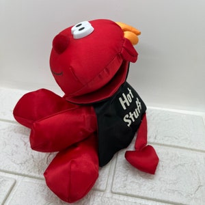Puede incluir: Juguete de peluche rojo con forma de diablo con una capa negra que dice "Hot Stuff".