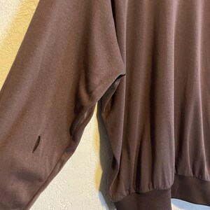 May include: A brown long-sleeved sweatshirt with a crew neck and ribbed cuffs. The sleeve has a small tear near the elbow. The fabric appears to be a soft, slightly worn material.