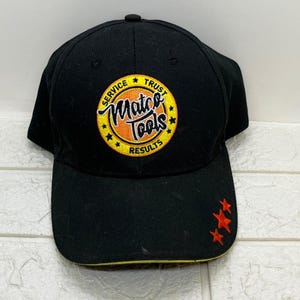 Può includere: Cappellino da baseball nero con visiera curva. Il cappellino presenta un logo ricamato con le parole "Matco Tools" in un cerchio giallo e arancione e le parole "Service, Trust, Results". Tre stelle rosse sono ricamate sul lato.