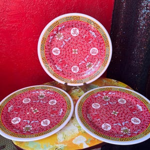 Op de afbeelding: Set van drie rood-witte decoratieve borden. Elk bord heeft een rode achtergrond met een wit bloemen- en wervelpatroon. De borden hebben een witte rand met een gouden geometrisch ontwerp en Chinese karakters.