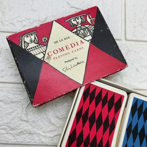 May include: A vintage "Comedia Playing Cards" box with a red, black, and white geometric design. The box features illustrations of figures and the text "De La Rue" and "Designed by Stig Lindberg". Playing cards with red and black diamond patterns are visible.