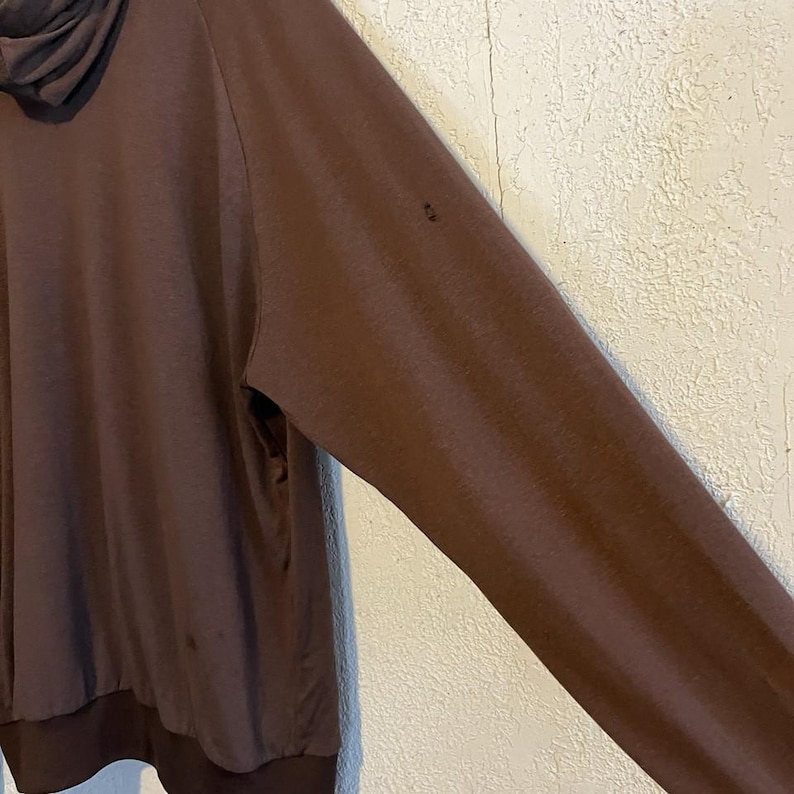 May include: A brown long-sleeved hooded sweatshirt. The sweatshirt has a dark brown hood and cuffs. The fabric appears to be soft and comfortable. The sleeve is angled towards the right side of the image.