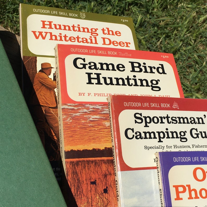 May include: A stack of vintage outdoor life skill books. Titles include "Hunting the Whitetail Deer," "Game Bird Hunting," and "Sportsman's Camping Guide." The books have red, green, and white covers with illustrations and text.