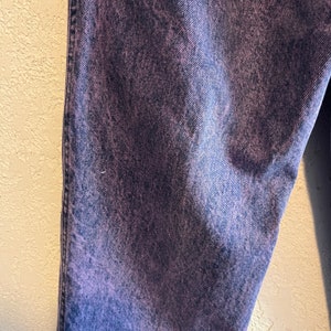 May include: Close-up of a pair of denim jeans with a purple and blue acid wash effect. The jeans have a classic five-pocket design and a straight leg cut. The fabric has a textured appearance.