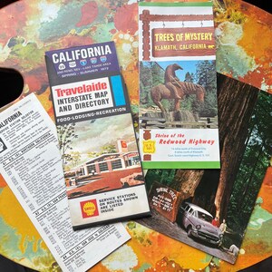 May include: A collection of vintage travel brochures and maps, including a 1972 California map and a guide to the Redwood Highway. Features a map for Trees of Mystery in Klamath, California.