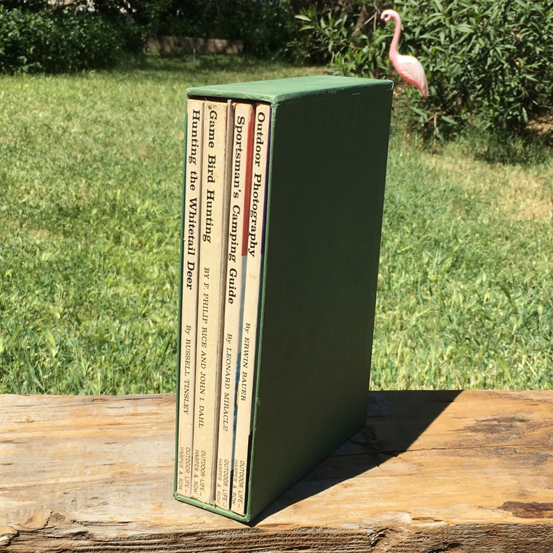 May include: A collection of vintage outdoor and hunting books in a green box. Titles include "Outdoor Photography," "Sportsman's Camping Guide," "Game Bird Hunting," and "Hunting the Whitetail Deer."