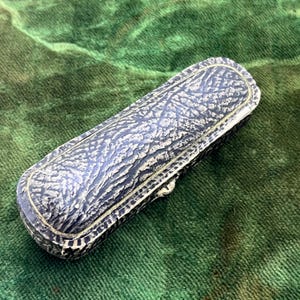 May include: A rectangular, vintage jewelry box with a textured, dark gray and white exterior. The box has a gold-colored trim and a clasp. The box is resting on a green velvet surface.