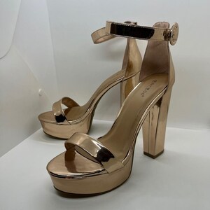 May include: A pair of rose gold platform heels with thick block heels and ankle straps. The shoes have a shiny, metallic finish and a buckle closure. The brand name "Bamboo" is visible on the inner side of the heel.