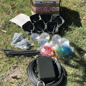 May include: A Ward Low Voltage Floodlight Kit containing six black light housings, six clear glass lenses, red, green, and blue plastic lens covers, black ground stakes, a black transformer with a coiled power cord, and an instruction manual.