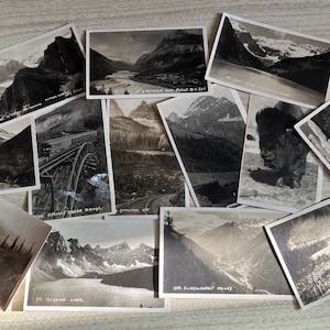 Puede incluir: Una colección de postales antiguas con vistas panorámicas de montañas, lagos y ríos. Las postales son en blanco y negro y tienen texto escrito a mano en el frente, incluyendo "Mt. Stephen and Field B.C. 205", "Sidney Creek Bridge", "Cathedral Mtn", "25B.  Illecillewaet Valley" y "Moraine Lake".