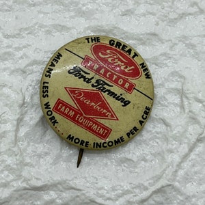 Puede incluir: Un botón vintage que anuncia equipos agrícolas de Ford Farming. El botón es redondo y presenta un logotipo de tractor Ford rojo y blanco con el texto "The Great New Ford Tractor" y "Ford Farming" en letras negras. El botón también presenta un diamante rojo con el texto "Dearborn" y el texto "Farm Equipment" en letras negras. El botón tiene el texto "Means Less Work... More Income Per Acre" en letras negras alrededor del borde.