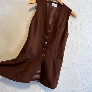Puede incluir: Un chaleco marr&oacute;n sin mangas con cuello en V, cinco botones redondos en la parte delantera y dos bolsillos inferiores ribeteados. La prenda incluye un bolsillo en el pecho y un forro interior marr&oacute;n con una etiqueta blanca BCBG Max Azria.
