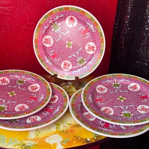 Op de afbeelding: Een set van zes rood-witte porseleinen borden met een traditioneel Chinees ontwerp. Elk bord heeft een centraal bloemmotief en Chinese karakters, omgeven door een decoratieve rand. De borden zijn op een tafel geplaatst.