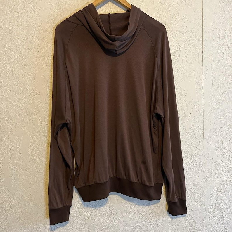 May include: A brown hoodie with long sleeves and a drawstring hood. The cuffs and hem are a darker shade of brown. The hoodie is made of a soft, lightweight material.