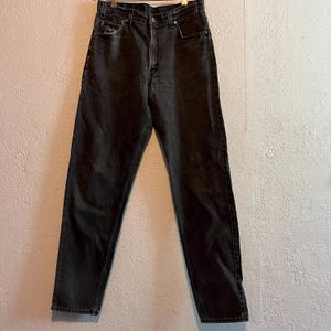K&ouml;nnte beinhalten: Hoch taillierte schwarze Jeans aus Denim mit klassischem F&uuml;nf-Taschen-Design, Metallknopfverschluss, Rei&szlig;verschluss und G&uuml;rtelschlaufen. Der Stoff hat eine leicht verwaschene Optik mit sichtbaren N&auml;hten entlang der Beinpartien.