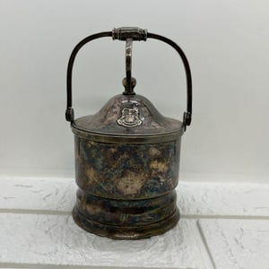 May include: Silver ice bucket with a lid and a handle. The bucket has a crest on the lid.