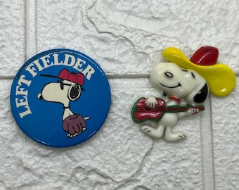 2 alfinetes vintage do Snoopy de amendoim. Cowboy de guitarra de plástico e jogador de campo esquerdo