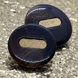 Puede incluir: Dos pendientes Escada azul oscuro con placas rectangulares doradas. Los pendientes tienen un acabado brillante y una forma redondeada. El fondo es de color dorado brillante.