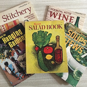 May include: A collection of five vintage Sunset books including titles Stitchery, Cooking with Wine, Ideas for Hanging Gardens, Salad Book, and Soups and Stews. The books feature illustrated covers with various food, garden, and craft themes.