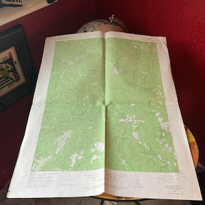 May include: An open vintage map of Big Basin, California, with green and white topographic details. The map is unfolded, showing a detailed landscape with roads and geographical features. The map is on a table with a globe in the background.