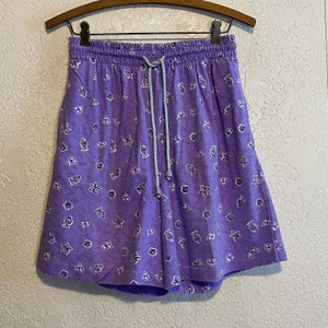 May include: Purple shorts with a white floral and fish print. The shorts have a drawstring waist.