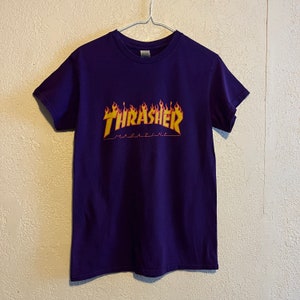 May include: Purple t-shirt featuring a yellow and orange "Thrasher Magazine" logo with flames.