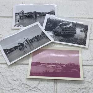 以下が含まれることがあります： 川に浮かぶ蒸気船を写した、ヴィンテージの白黒写真のコレクション。1枚はピンクがかった色合いです。画像は、質感のある白い表面に配置されています。