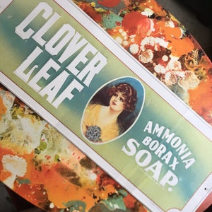 Può includere: Insegna vintage di Clover Leaf Ammonia Borax Soap. L'insegna rettangolare presenta un ritratto di donna e il nome del prodotto in lettere bianche su sfondo verde e blu. L'insegna ha un bordo bianco.
