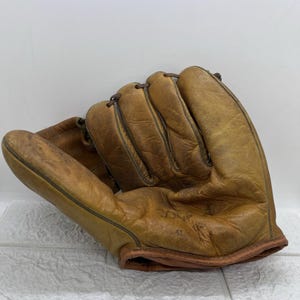 May include: A well-worn, brown leather baseball glove. The glove shows signs of use with visible creases and wear marks. The stitching is a darker brown, and the glove has a pocket for catching the ball. The glove is designed for a right-handed player.