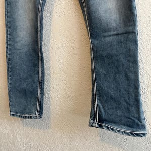Pu&ograve; includere: Jeans in denim blu sbiadito con cuciture bianche lungo le cuciture. I jeans hanno un leggero svasatura sul fondo. Il denim ha un aspetto usurato.