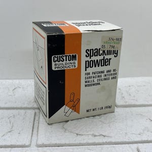 May include: A vintage box of spackling powder from Custom Building Products. The box is white with black and orange accents, and features the text "spackling powder" and "for patching and resurfacing interior walls, ceilings and woodwork." Net weight is 1 lb (453g).