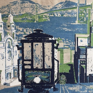 May include: A fabric print featuring a stylized depiction of San Francisco. The design includes a cable car, the Golden Gate Bridge, buildings, and hills, rendered in shades of blue, green, and beige. The overall aesthetic is reminiscent of vintage travel posters.