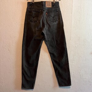 K&ouml;nnte beinhalten: R&uuml;ckansicht einer verblichenen schwarzen Jeans. Die Jeans hat ein klassisches F&uuml;nf-Taschen-Design, mit dem Levi's-Markenaufn&auml;her auf dem Bund. Das orangefarbene Levi's-Etikett befindet sich auf der Ges&auml;&szlig;tasche. Die Jeans h&auml;ngt an einem Kleiderb&uuml;gel.