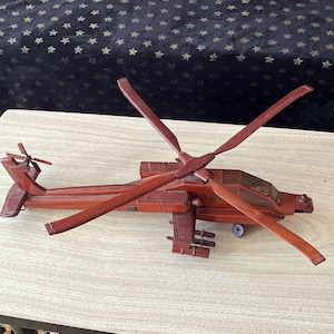 May include: A wooden model of an Apache helicopter with a dark brown finish. The model has a detailed design and is a great addition to any military enthusiast's collection.