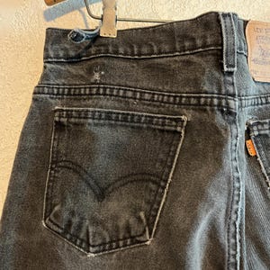 K&ouml;nnte beinhalten: Nahaufnahme der R&uuml;ckseite einer verblichenen schwarzen Jeans. Die Jeans hat ein klassisches F&uuml;nf-Taschen-Design mit einer Ges&auml;&szlig;tasche auf der linken Seite. Das Markenetikett von Levi's ist auf der rechten Seite sichtbar. Die Jeans ist abgenutzt, mit Gebrauchsspuren.