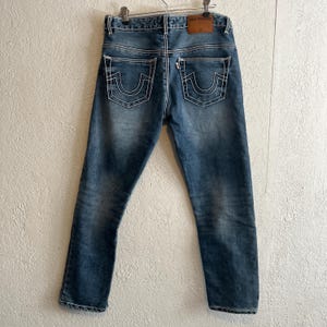 Pu&ograve; includere: Jeans blu in denim con dettagli di cuciture bianche. I jeans hanno un classico design a cinque tasche, una toppa in pelle sul retro e una chiusura con bottone in metallo. Le tasche posteriori presentano un caratteristico design con cuciture curve.