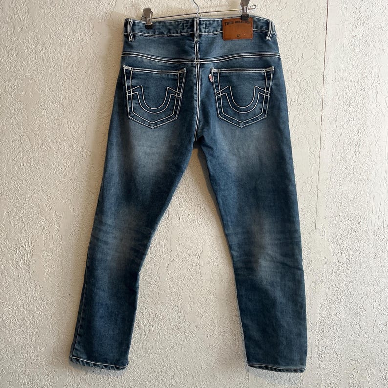 Pu&ograve; includere: Jeans blu in denim con dettagli di cuciture bianche. I jeans hanno un classico design a cinque tasche, una toppa in pelle sul retro e una chiusura con bottone in metallo. Le tasche posteriori presentano un caratteristico design con cuciture curve.