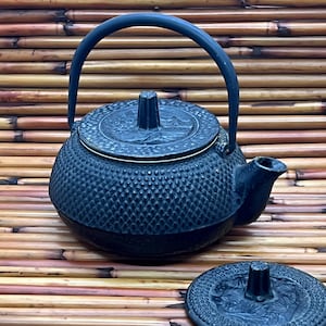 May include: A dark blue cast iron teapot with a textured surface and a curved handle. The lid features a decorative design. The teapot is designed for brewing tea and has a spout for pouring.