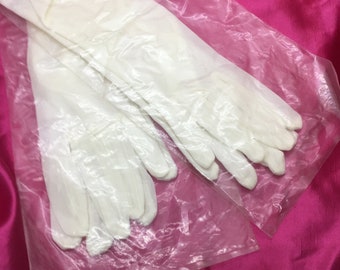 May include: A pair of long, cream-coloured gloves, packaged in a clear plastic bag. The gloves appear to be made of a lightweight material. The background is a vibrant pink fabric.