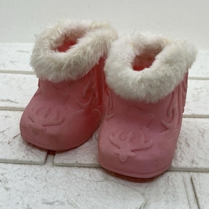 May include: A pair of pink baby boots with white faux fur trim. The boots have a decorative embossed design on the front and sides. The boots are designed for infants and are made of a soft material.