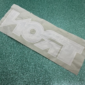 May include: A white iron-on transfer decal featuring the word KOKT in a bold, blocky, sans-serif font. The letters are outlined and appear as a single adhesive piece on a translucent backing sheet, ready for application onto a fabric surface.