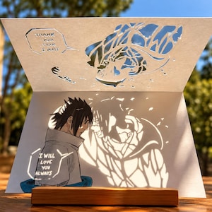 May include: A white paper cutout card featuring a detailed illustration of a character with spiky dark hair. The card includes text bubbles that read THANK YOU FOR I WAIT and I WILL LOVE YOU ALWAYS. The design casts a complex shadow on the paper.