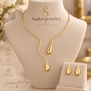 May include: A gold-toned necklace and earring set featuring a curved, open-ended collar necklace with two dangling teardrop pendants. The set includes matching teardrop stud earrings. The text SadoraJewelry is visible at the top and bottom.