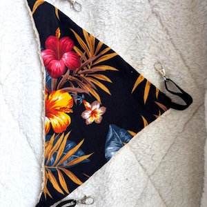 May include: A triangular pet hammock featuring a black fabric base with a vibrant tropical print of red and yellow hibiscus flowers and golden palm leaves. The edges are lined with white fleece, and three black straps with silver metal clips are attached.